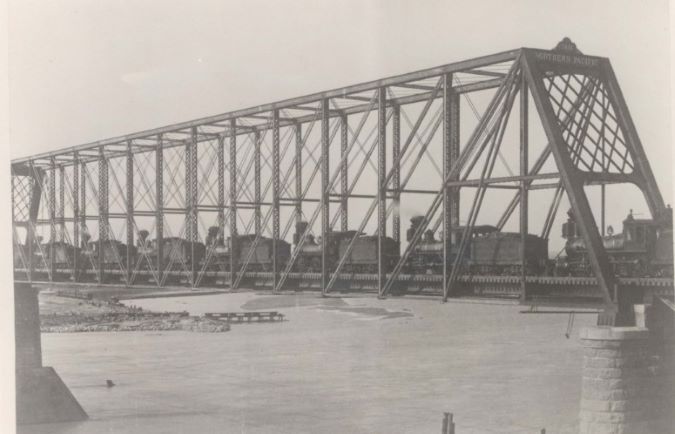 A string of steam locomotives crosses the bridge in the late 1800s.